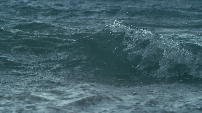 Dark choppy ocean waves churn and splash under driving rain