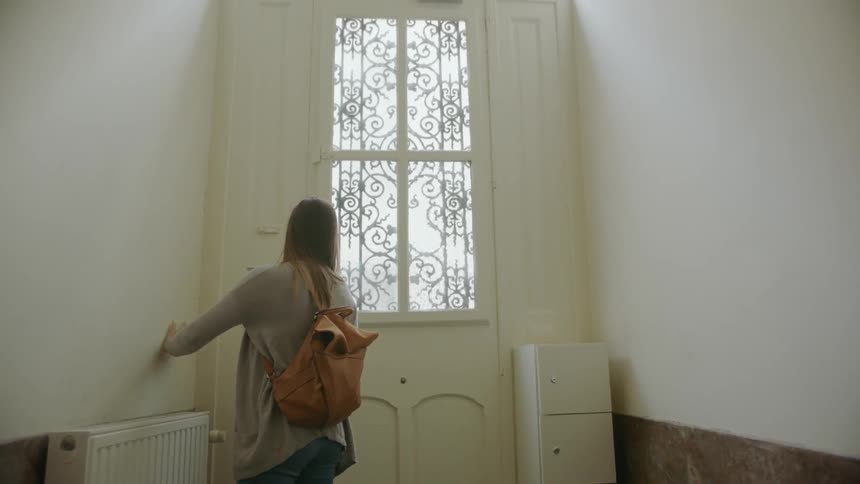 A woman walks down a hall and grabs a door handle