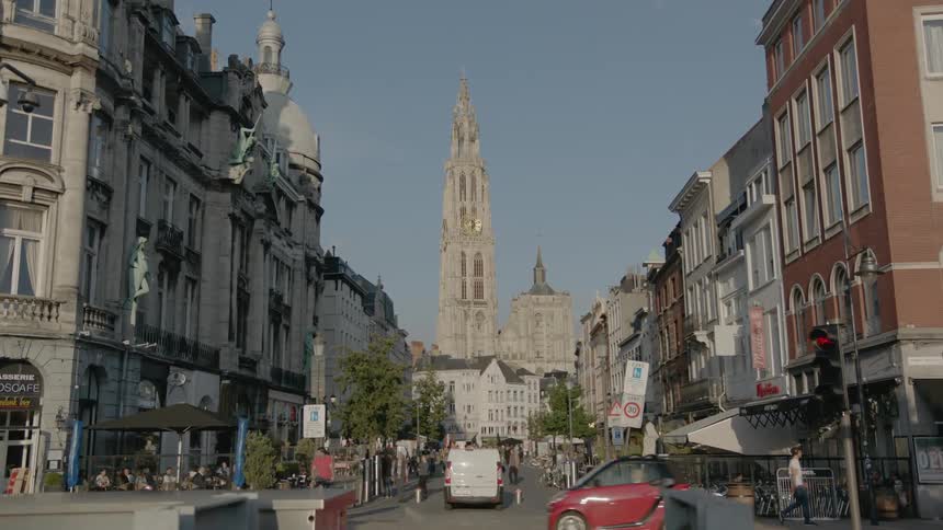 A view of a city with large ancient looking buildings and people walking around