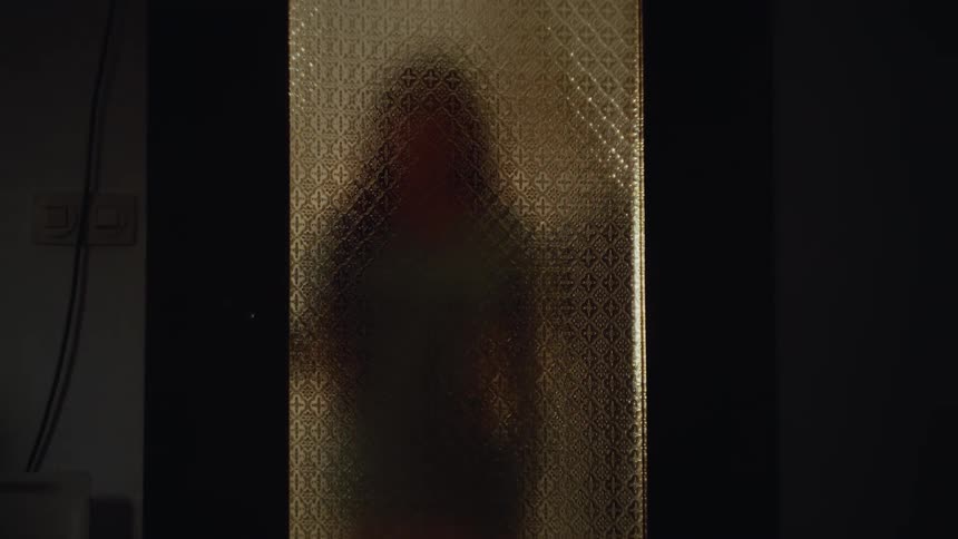 A silhouetted figure stands behind a textured glass door in a dimly lit setting