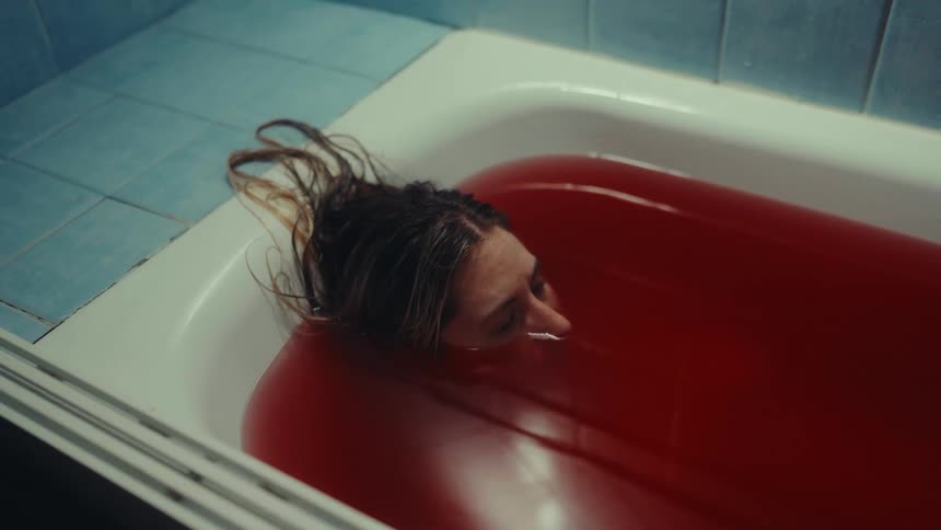 Woman in red filled bathtub with face partially submerged