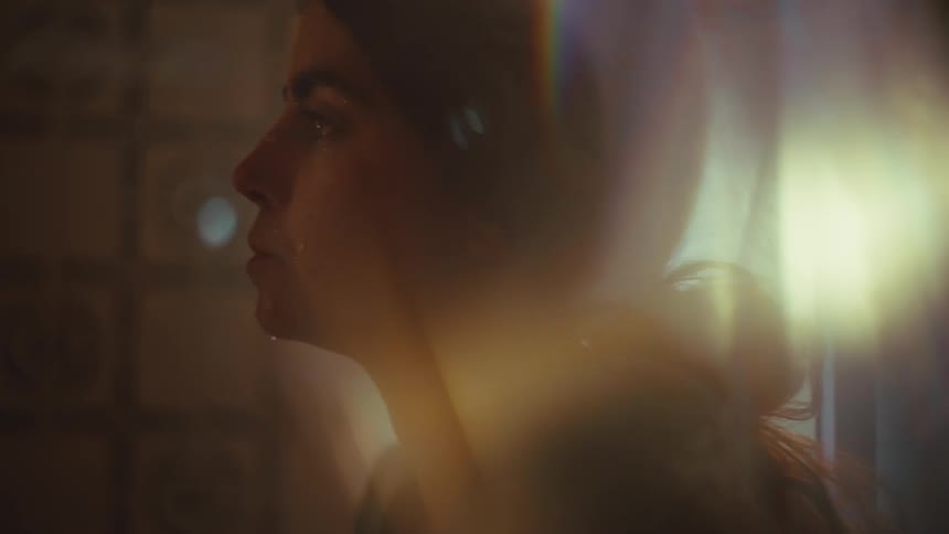 A woman in low light ties her hair appearing slightly sad or disturbed
