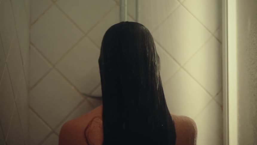 A woman with long black hair is taking a shower in the bathroom at midday