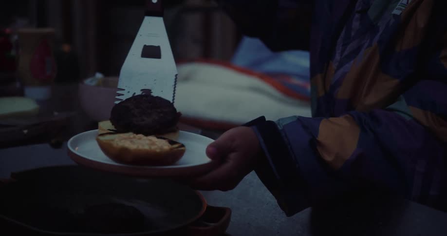 A person serves food onto a plate in dim lighting