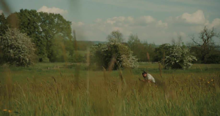 Person in white crouching in a field surrounded by trees