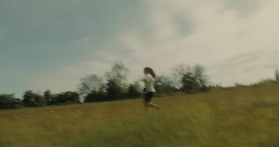 Woman with open arms walking through a field with trees in the background