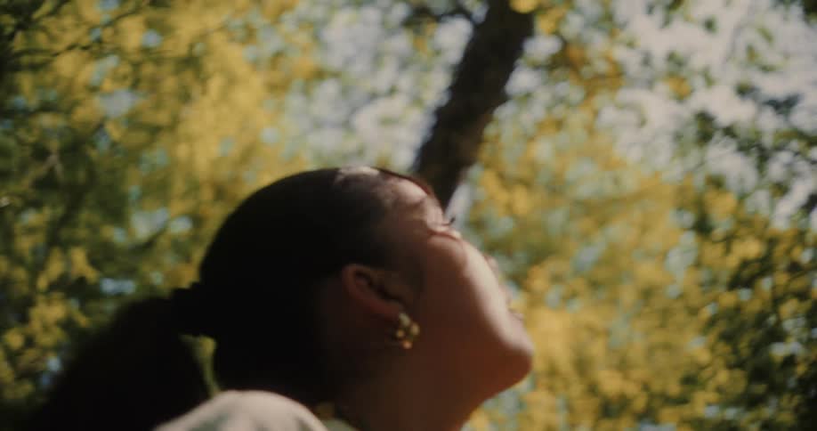 Woman with her hair tied up and a backpack on her back in the middle of a forest looking up with the reflection of the sun