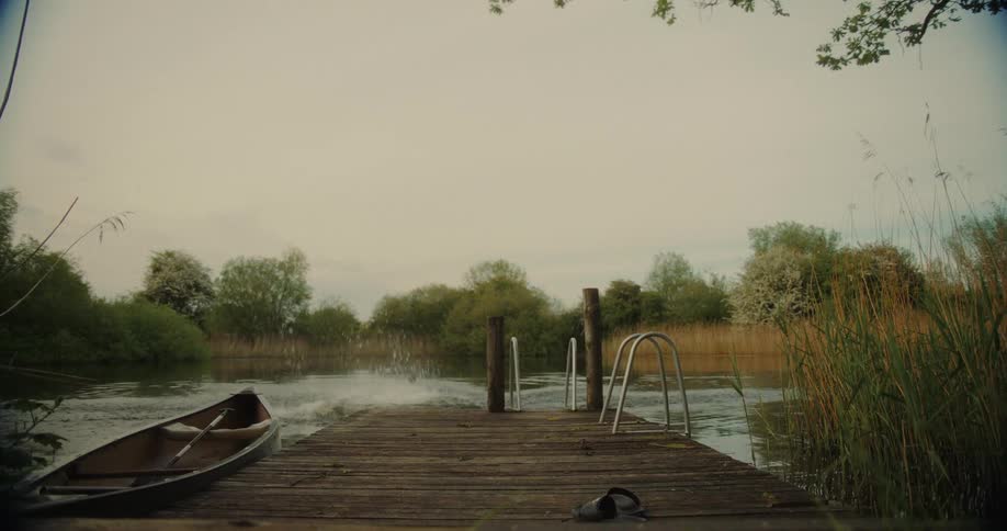 Man in swim trunks running down wooden pier and jumping into lake with another person