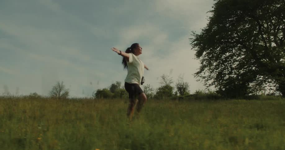 Woman opening her arms and walking through a field with trees around her