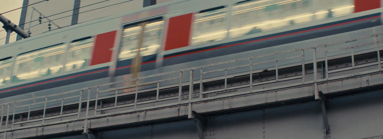 The video displays a side view of a monorail passing by with red and white cars moving quickly across the frame the camera is positioned below the tracks capturing the train as it crosses an elevated structure