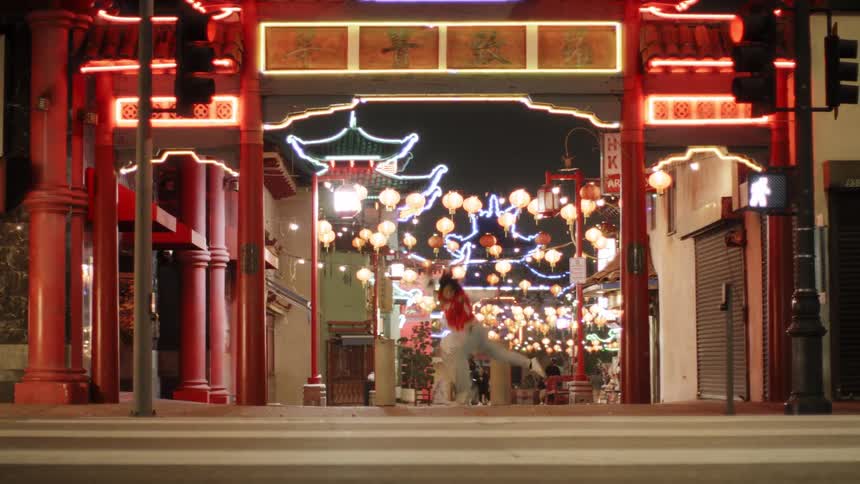 A young man dances under red lanterns at chinatowns brightly lit entrance surrounded by glowing signs and festive street decor