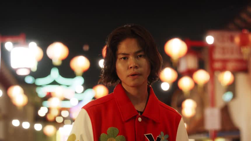 An Asian teenager  is standing in the city at night
