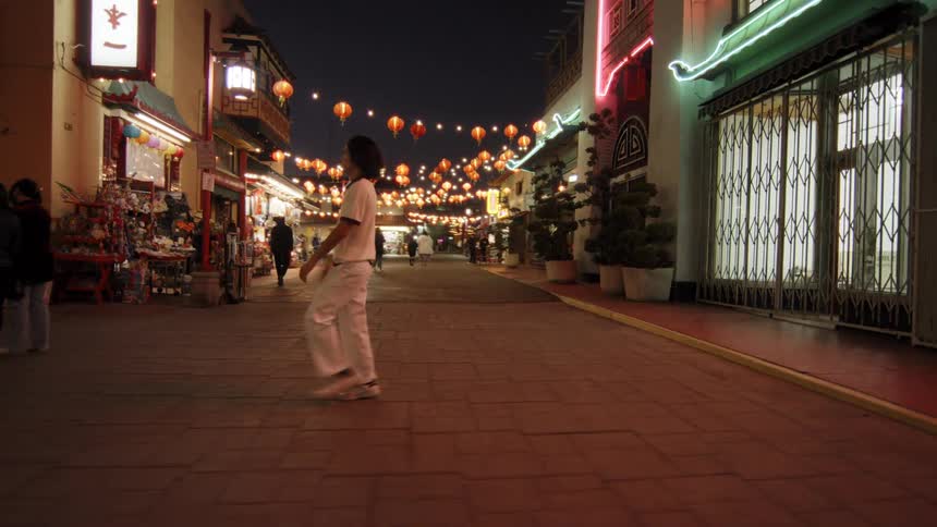 A person dressed in white performs a high kick on a brightly lit street adorned with red lanterns and festive decorations