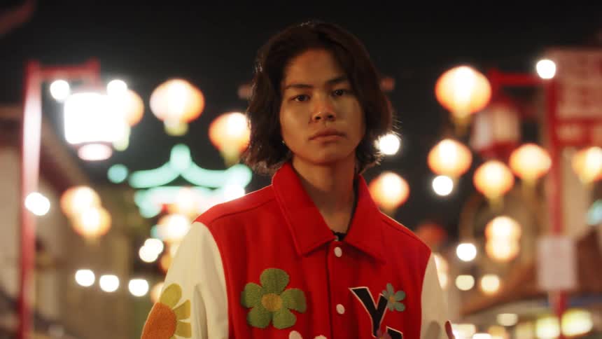 Young man wearing a jacket decorated with flowers stands in a street decorated with chinese lanterns at night