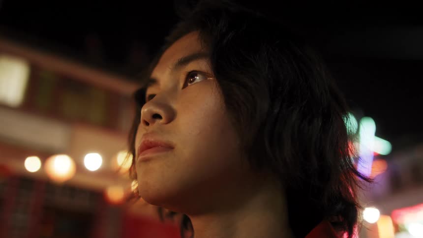 An Asian teen looks around in a city at night
