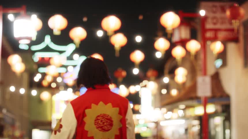 A young Asian teen model stands in Chinatown at night then walks away