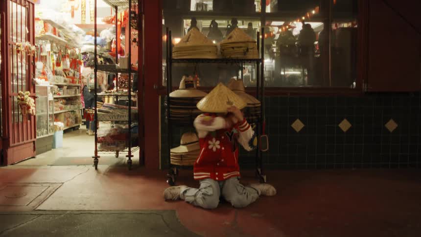 Young teen dancing in a solo performance in an outdoor setting next to a store and putting on a hat