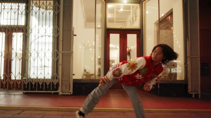 Young man dancing in a solo performance next to closed shops at night