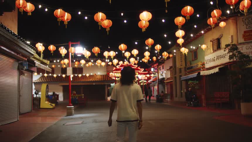 Male pedestrian walks along a street decorated with hanging chinese lanterns at night