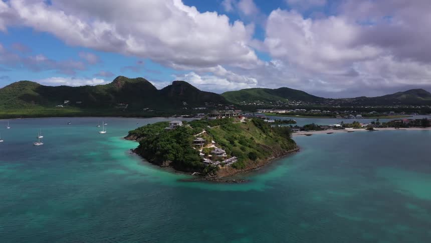 An island is surrounded by the ocean with sailboats in the water at midday