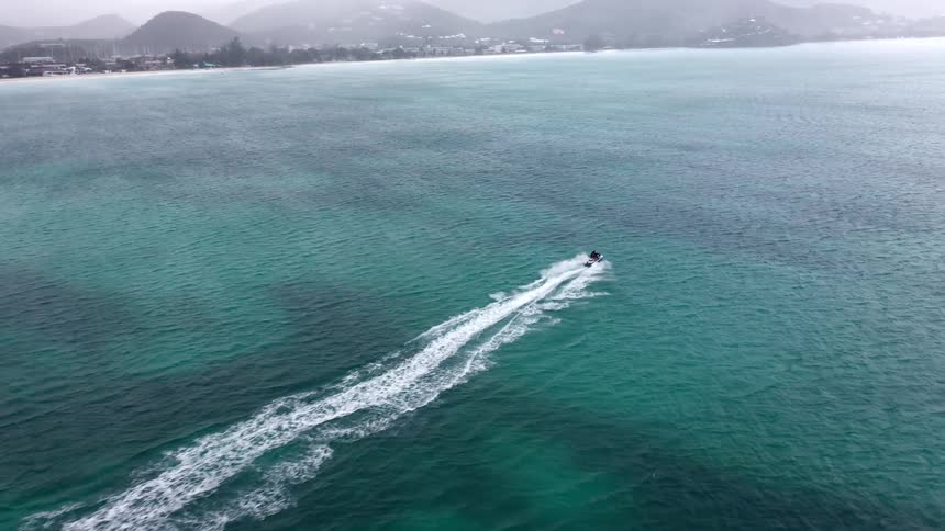 Person rides a jet ski through the ocean a significant distance from a coastal town leaving a long wake on a foggy day