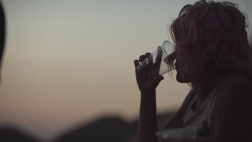 Three people including one woman are drinking alcohol from cups at sundown