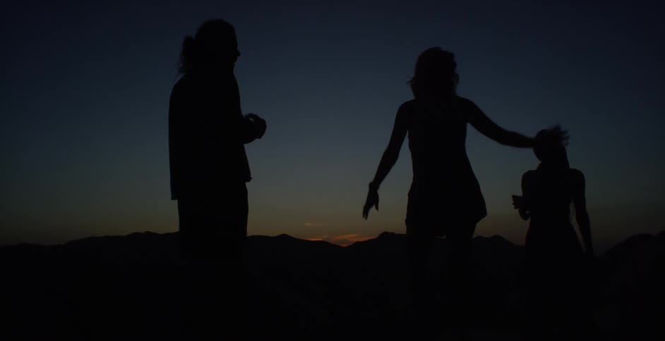 Silhouette of three people in an outdoor setting at dusk