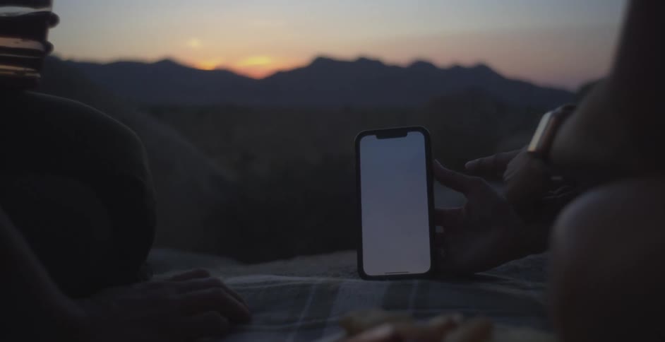 Person holding a smartphone while standing outdoors at dusk