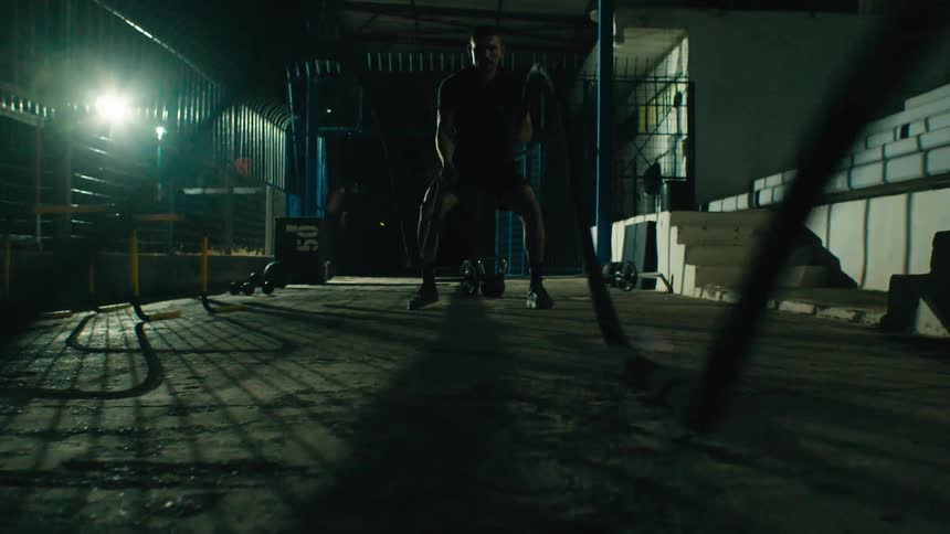 A man is pulling ropes in the dark gym for exercise