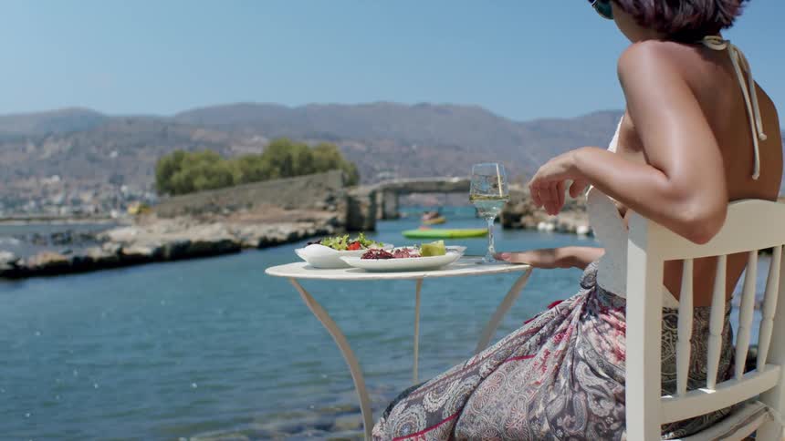 A woman on vacation is having food and drinks by the water