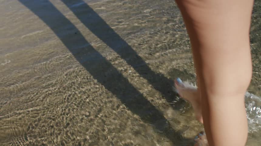 Legs of a woman walking on the shore of the sand and sea on the beach