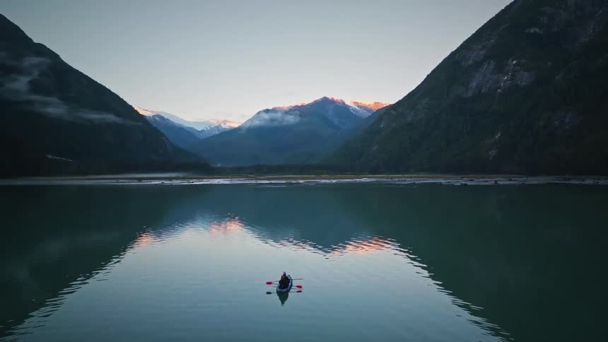 A person is riding a canoe on a lake surrounded by mountains