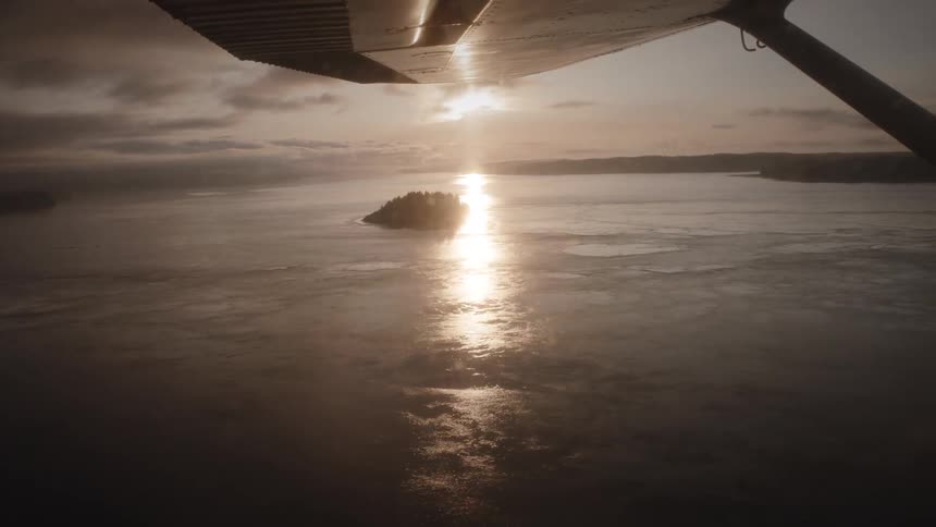 A plane flies over the water as the sun rises