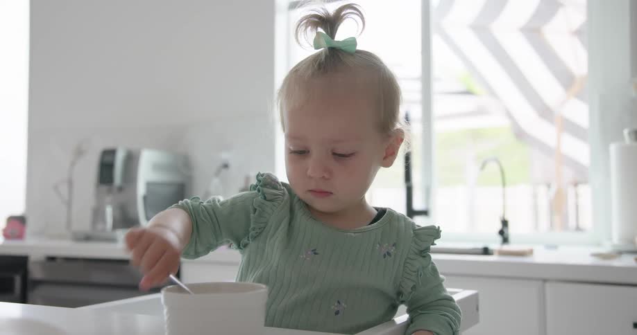 A child playing with her food while seated in the kitchen