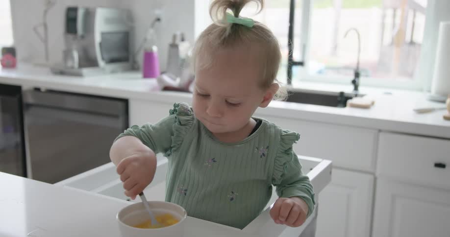 Little baby girl holding a fork in a container with liquid on the table
