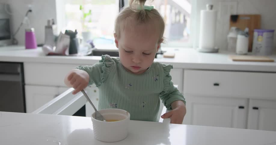 Baby sitting at the table and stirring liquid food in a bowl