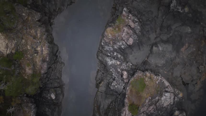 A stream flows through a mountain with trees growing on top of the rocks at midday