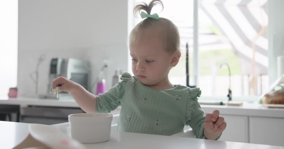 Female baby plays with beaten egg with a fork in a bowl placed on a counter top in the kitchen during daytime