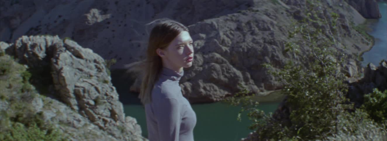 A woman is standing on a cliff with a visible lake below