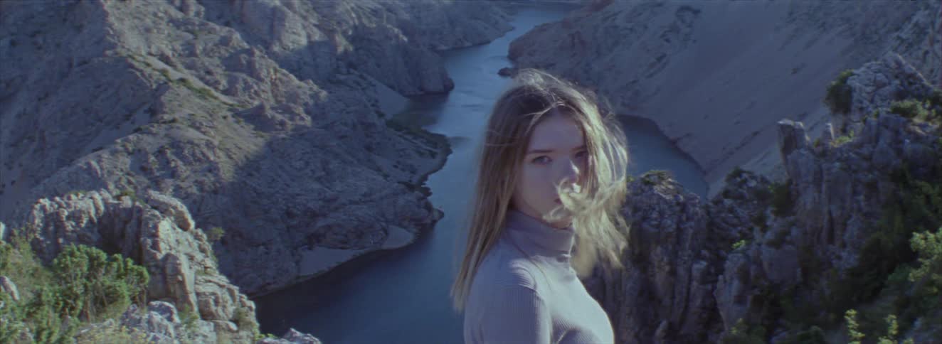 A woman stands looking out over a river in a valley