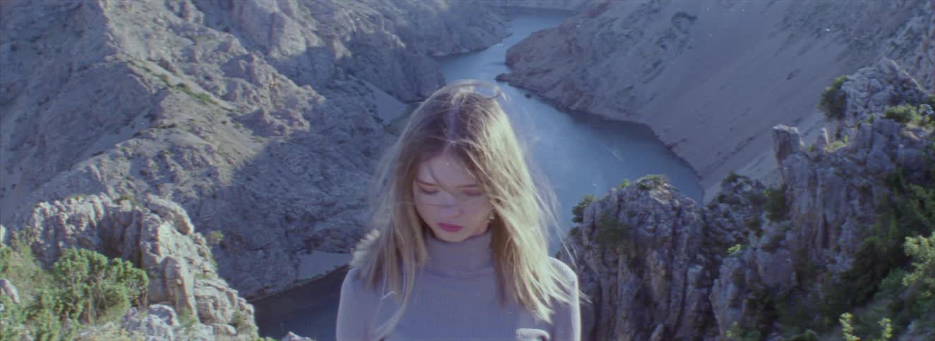 Young blonde woman with her hair blowing in the wind against a backdrop of mountains and a river