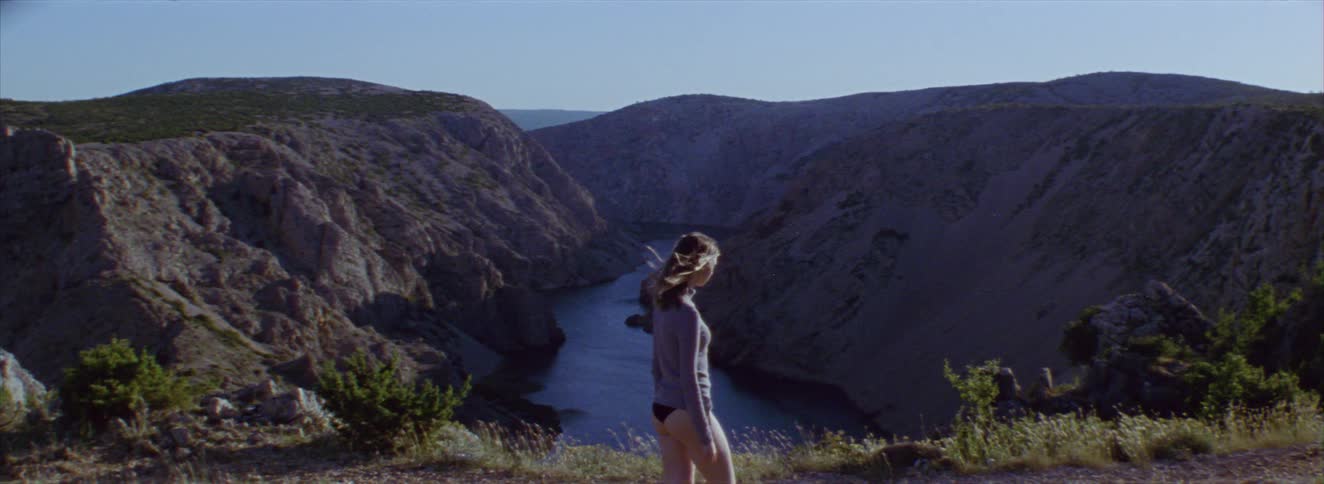 Woman in a tshirt and underwear walking through the mountains with a river in the background