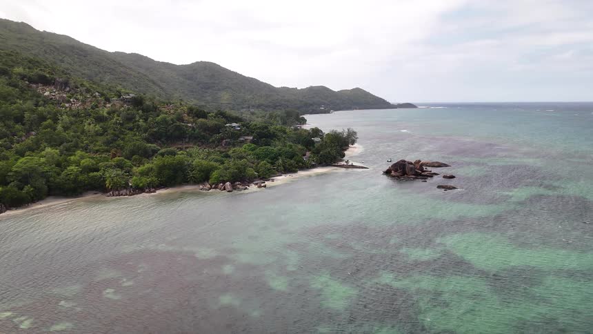 A coastal landscape featuring lush green hills a rocky shoreline and clear turquoise waters extending to the horizon