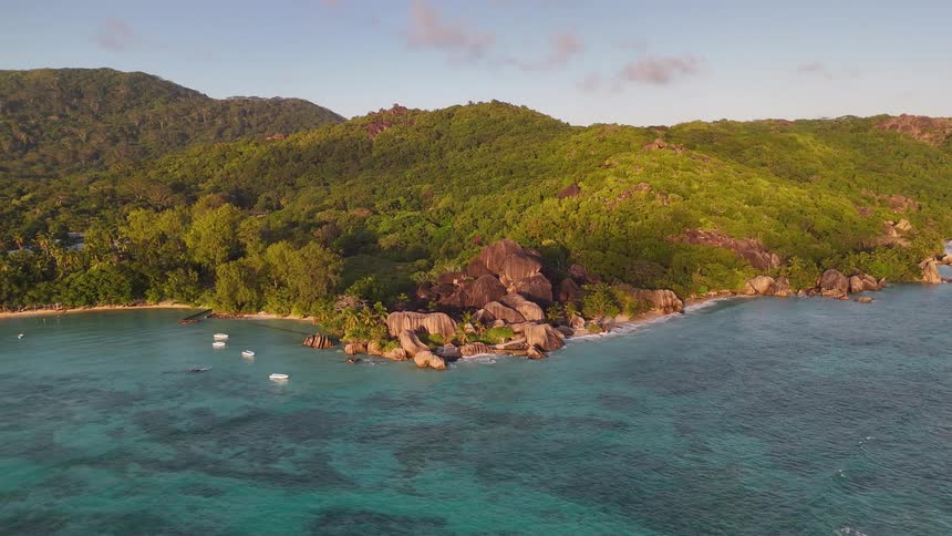 A mountainous island covered with vegetation with boats docked along the shoreline