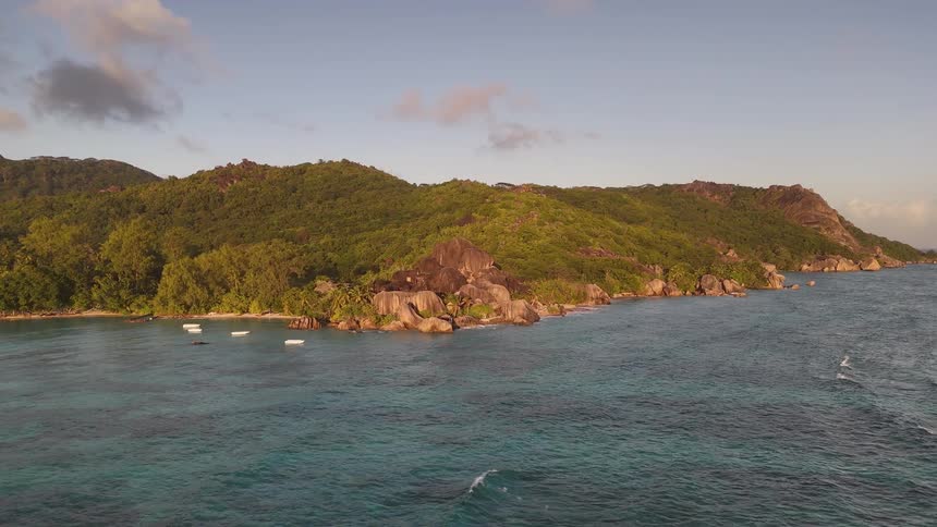 Several small boats float near the rocky shoreline of a lush green island surrounded by clear blue waters