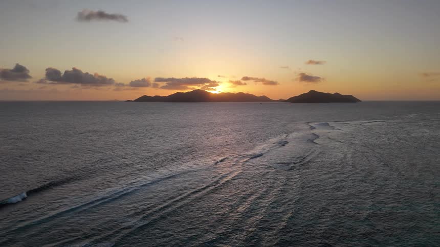 Waves shimmer in soft twilight as they roll gently toward the coast where a distant island stands silhouetted on the horizon