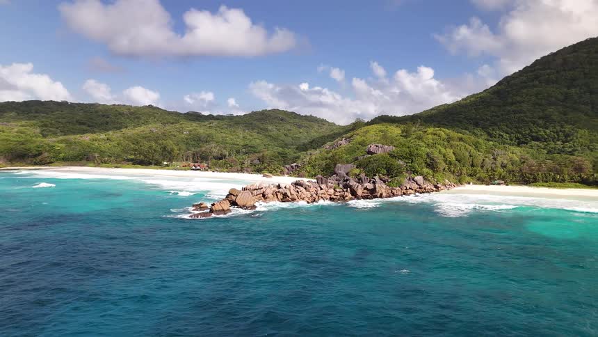A sweeping aerial shot pans across a stunning tropical coastline centered on a rocky point that separates two white sand beaches