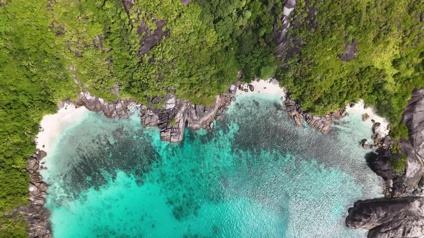 Aerial view of a secluded cove reveals vibrant turquoise waterand lush green cliffs surrounding hidden beaches