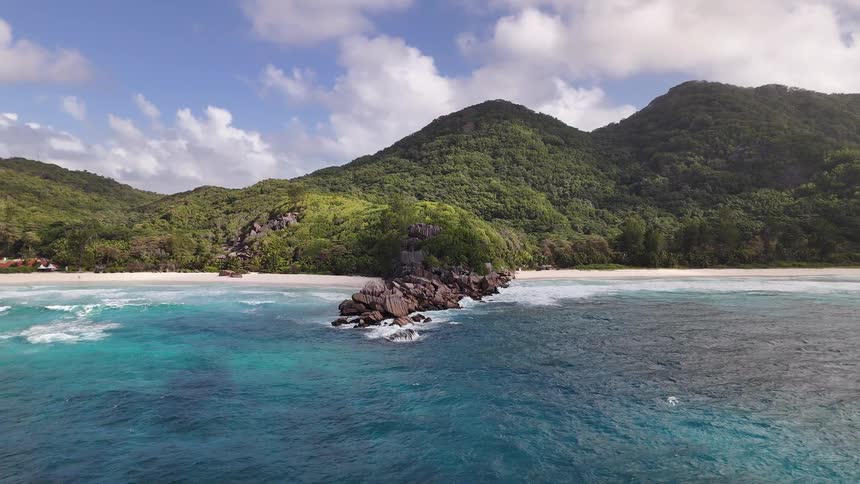 Lush green mountains meet a turquoise ocean at a tropical rocky beach