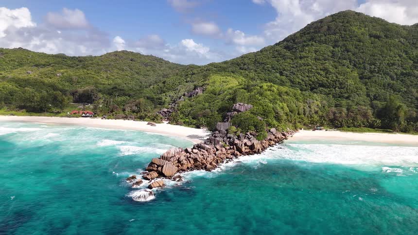 A rocky formation juts into the turquoise sea flanked by white sand beaches and lush green mountains